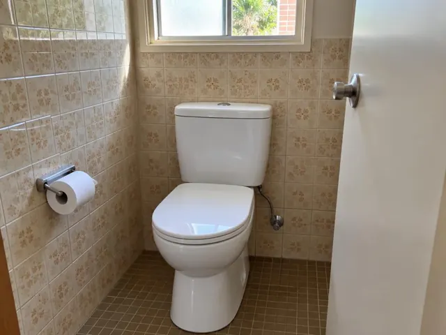 Clean white toilet in a tiled bathroom with a small window in Collaroy