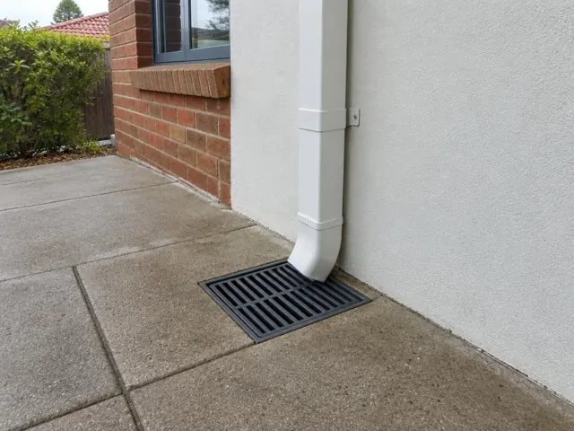Concrete driveway beside a brick wall with a clean stormwater grate under a downpipe in Cromer
